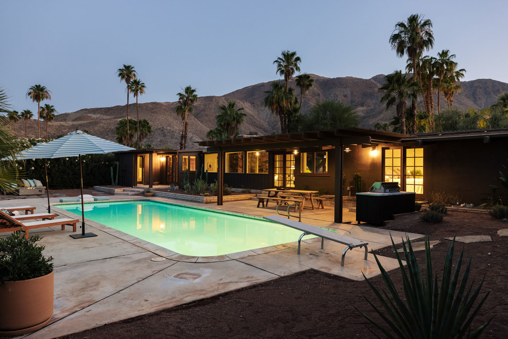 7153 Biskra Rd - Backyard at dusk with lit up pool and mountains in the background